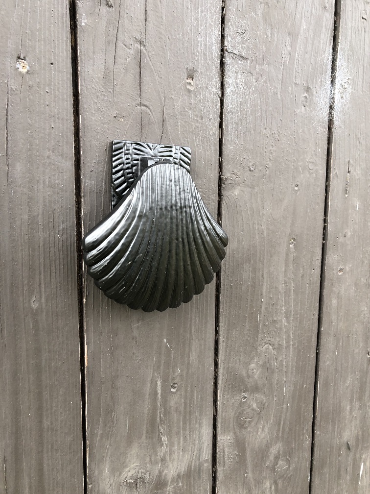 Decoratieve deurklopper in de vorm van een schelp, geheel metaal zwart.